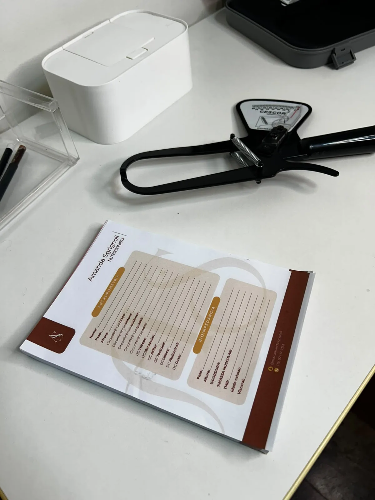 Materiais de avaliação corporal, com adipômetro e ficha de anamnese