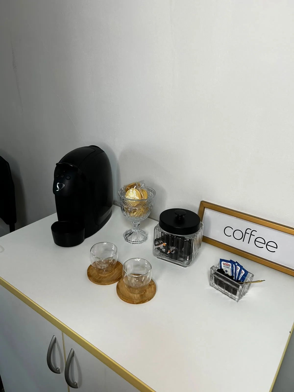 Estação de café do consultório, com cafeteira, xícaras e docinhos